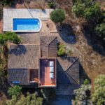 Aerial view of a house with a terracotta roof, a rectangular blue pool to the top left, and surrounding trees and yard.