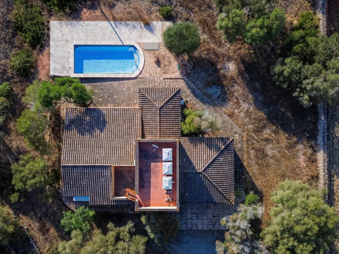 Aerial view of a house with a terracotta roof, a rectangular blue pool to the top left, and surrounding trees and yard.